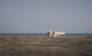 Daytime view of the library in the distance, grassy sand dunes, sea, and and clear blue sky