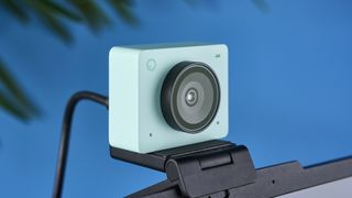 a photograph of a 1 inch wide mint webcam with a 4K sensor and built-in microphone, photographed against a blue background