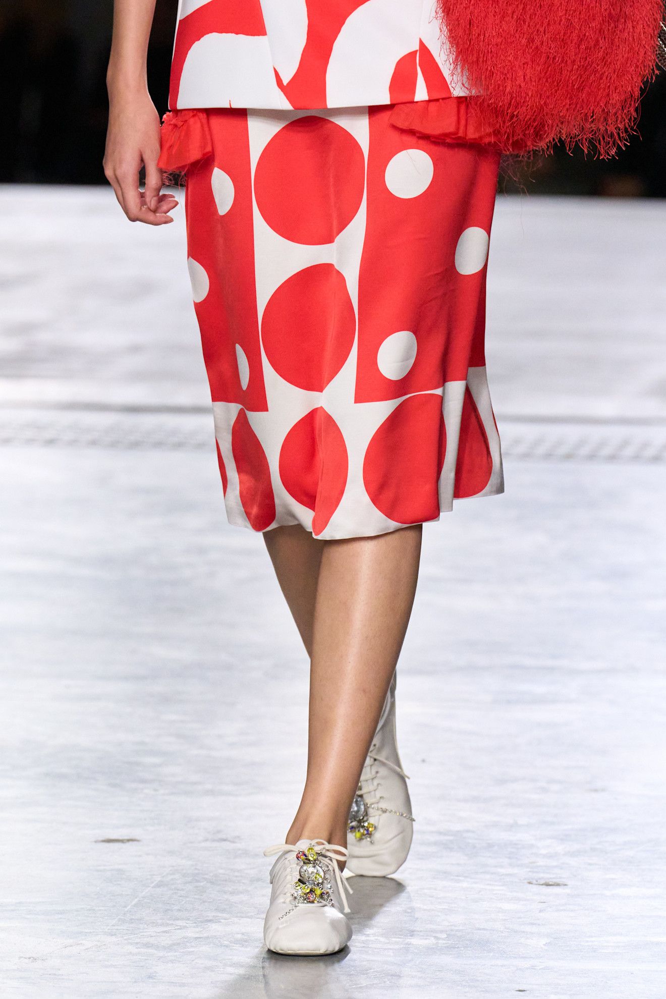 A model at the spring/summer 2026 Dries Van Noten show in Paris wearing a patterned skirt and white low-profile sneakers with beads on the laces.