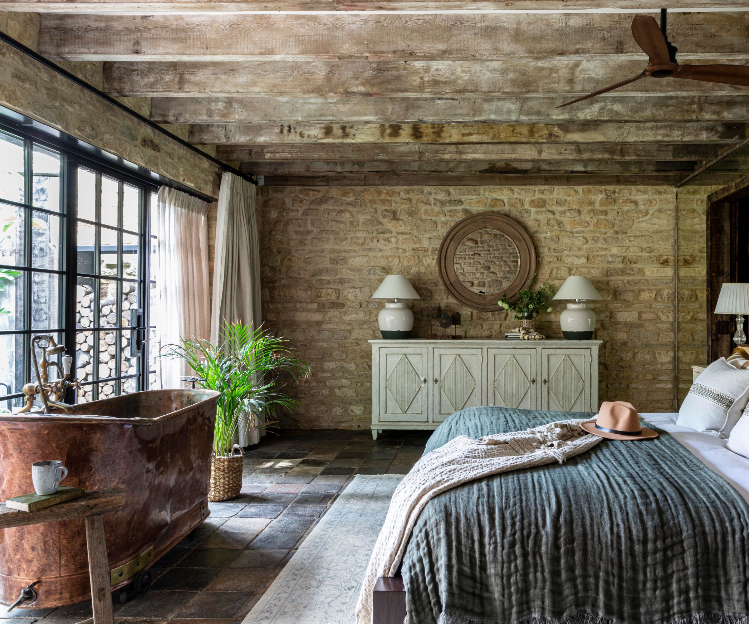 A countryside bedroom with exposed brick walls and a copper freestanding bath