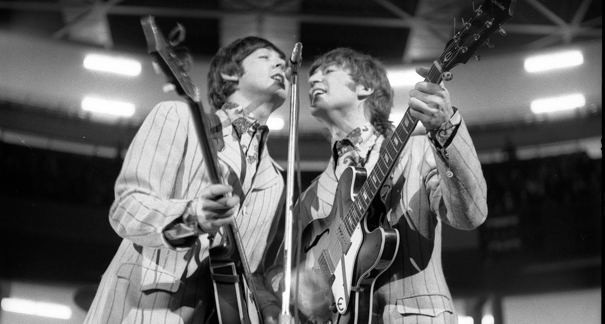 A black-and-white image of Paul McCartney and John Lennon in striped suits, sharing the mic at Olympia Stadium, 1966.