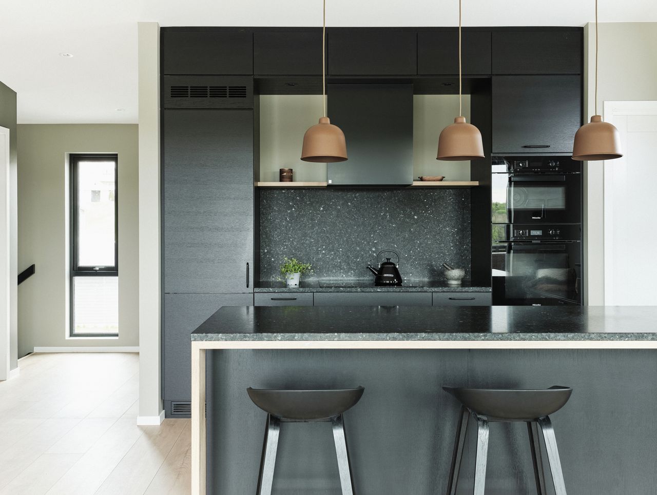 A dark themed kitchen with terracotta pendant lights