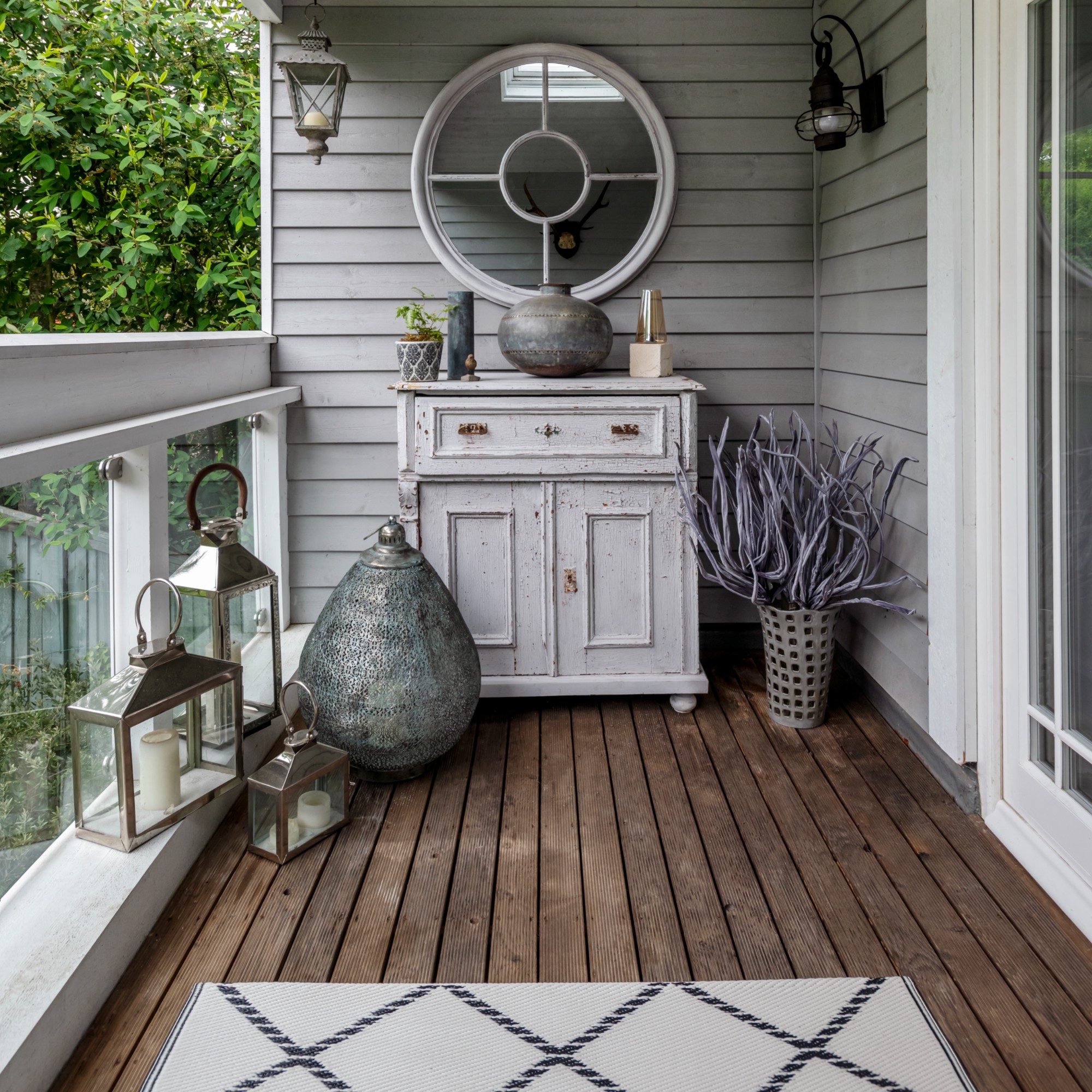 A balcony with panelled walls painted grey and dark wood flooring with an antique wooden cabinet displaying decorative items