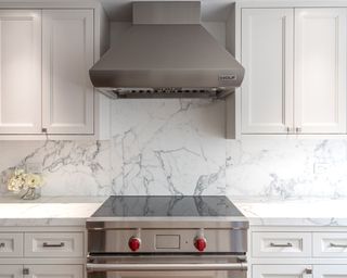 Kitchen with range and hood, white cabinets and veined stone backsplash