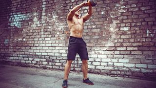 Athletic man working out with a kettlebell in front of brick wall. Outdoor workout.