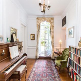 music room with piano, white French doors, bookcase and green armchair