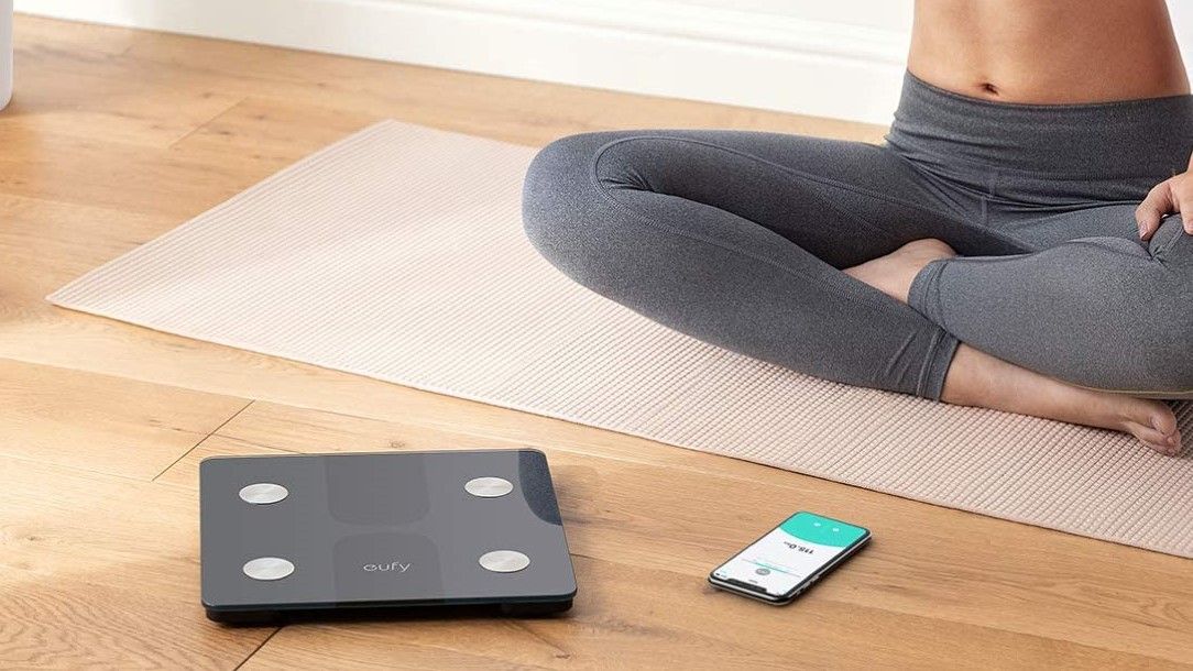 Woman sitting on the floor beside Eufy Smart Scale C1