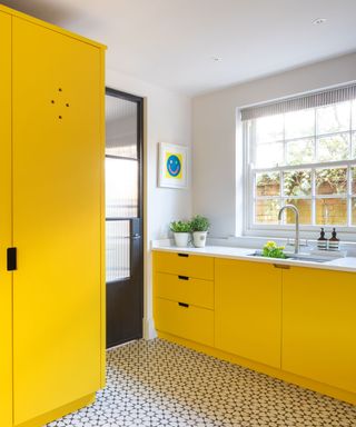 A utility room with bright yellow cupboards and a monochrome patterned floor.