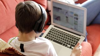 A young boy wearing headphones and relaxing on the couch while using a laptop to browse the web