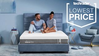 Tempur-Pedic mattress sales: A smiling couple sit on the Tempur-Pedic Tempur Cloud Mattress placed in a light blue bedroom