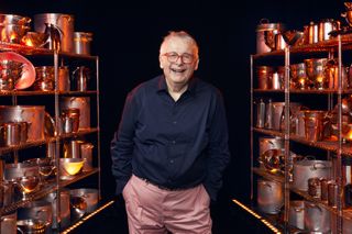 Christopher Biggins standing in between two racks of cooking equipment, filled with saucepans and colanders