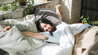 A young woman waking up happily and stretching in bed as the morning sunlight streams into her bedroom.