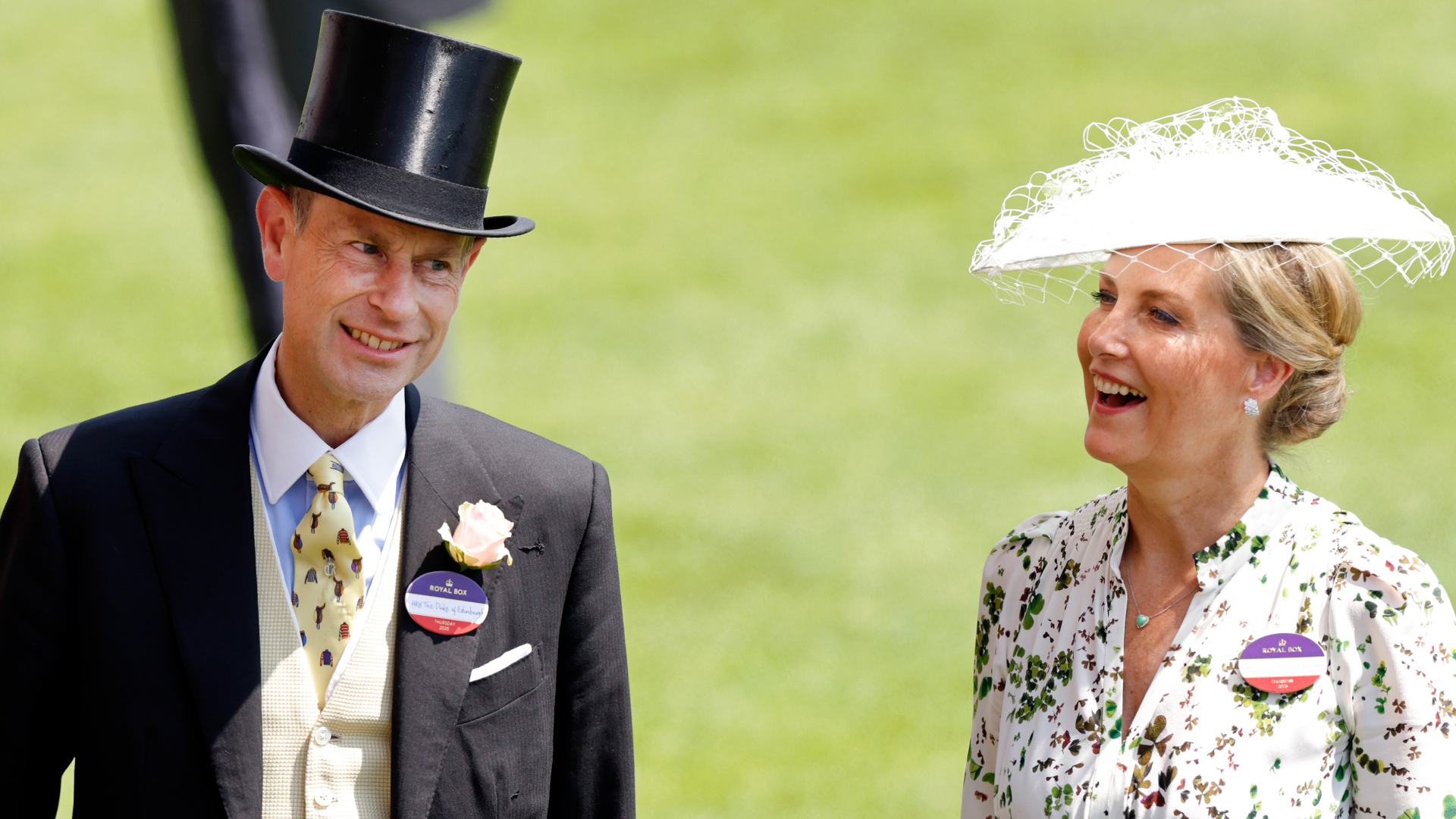 Duchess Sophie wearing a white hat and floral dress and Prince Edward in a top hat and suit smiling at Royal Ascot 