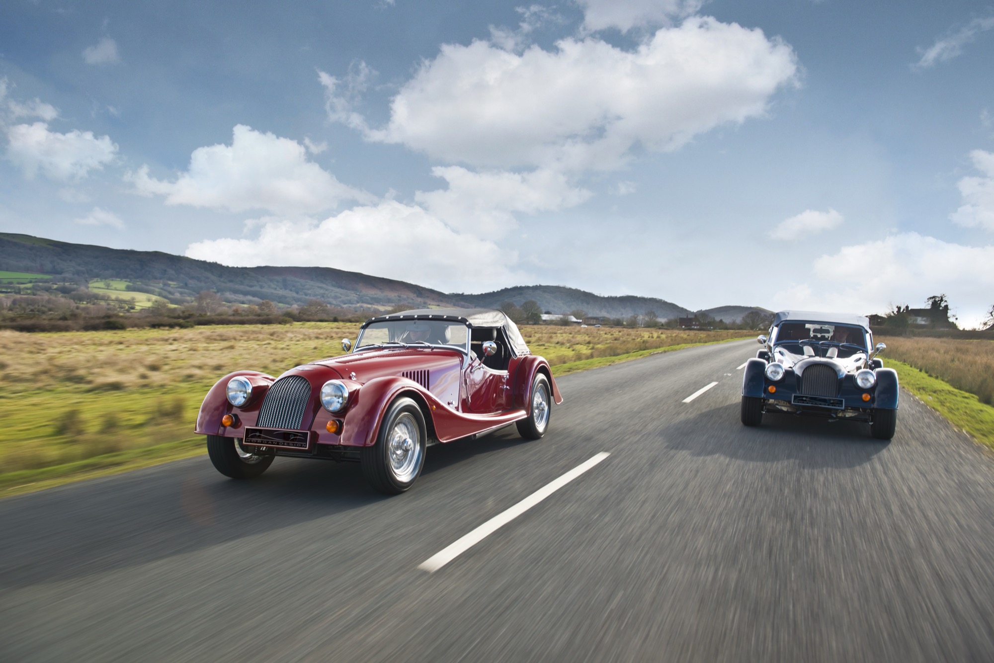 Two Morgans driving down a road, one red and one blue
