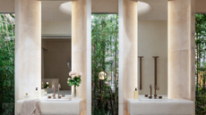 a his and hers sink in front of a glass wall with two backlit mirrors