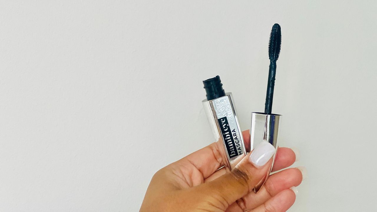 A person holding an opened silver L'Oreal Bambi Eye mascara tube for the best L'Oreal mascara.