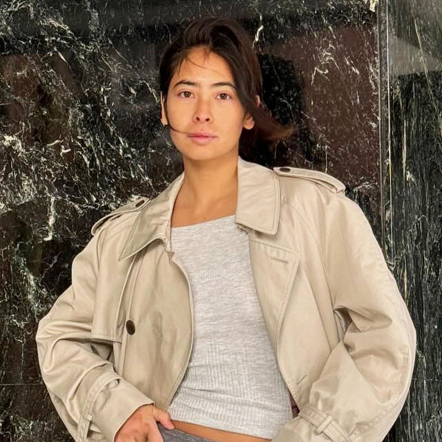 Michelle Li wearing a tan trench coat, grey top, grey sequin skirt, and black sneakers