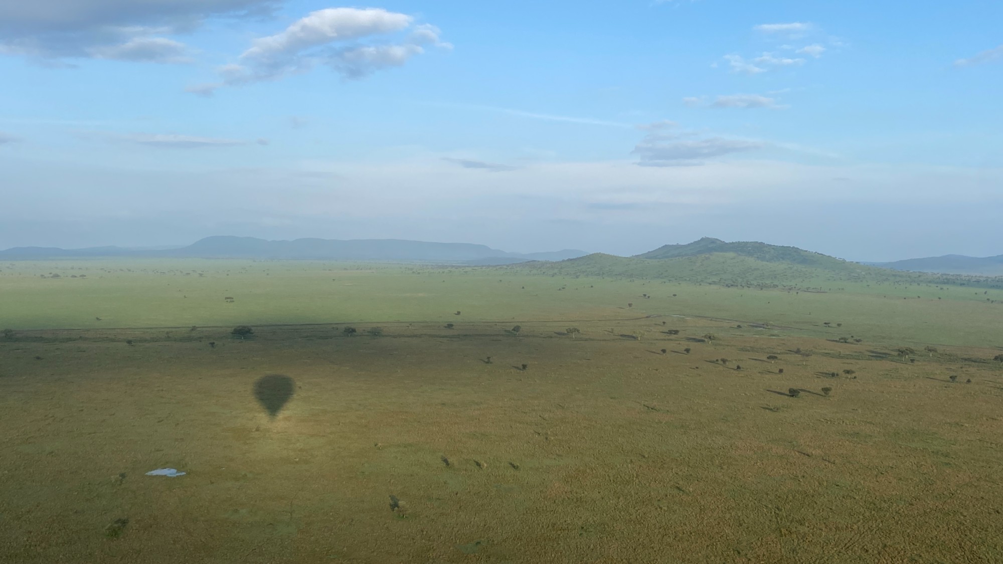 Serengeti national park from air with shadow of hot air balloon in foreground and mountains in background
