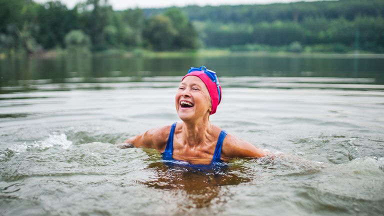 older woman in a swim cap enjoying the mental benefits of cold water swimming in a lake