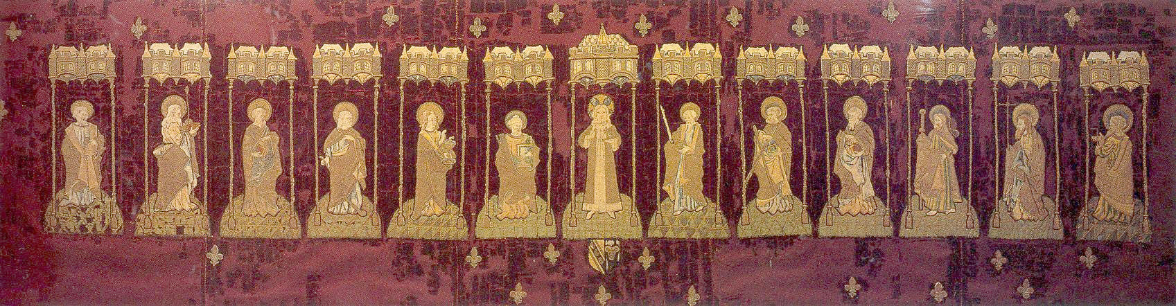 Altar frontal showing Christ and the twelve apostles, on dark crimson velvet. Bearing the arms of Sir Piers Edgcumbe and his wife Joan Durnford, who married in 1493; she died in c.1521). Each figure stands under a Gothic canopy of two oriel windows supported by thin poles. A scattering of fleur de lys over the background.