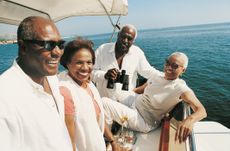 Two older couples are smiling on a boat. One holds binoculars. There is a tray with champagne or wine in glasses.