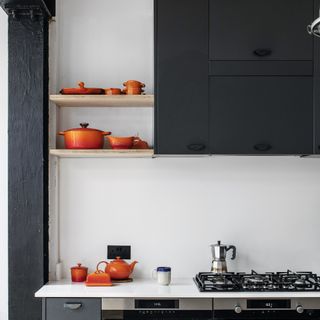 White painted kitchen with black kitchen cupboards, open shelving displaying orange Le Creuset cookware