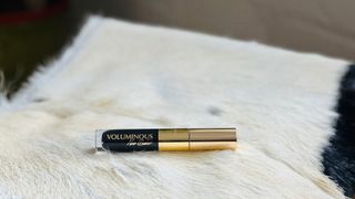 A gold and black L'oreal mascara tube laying on a furry stool, for L'oreal Voluminous Noir Balm Mascara review.