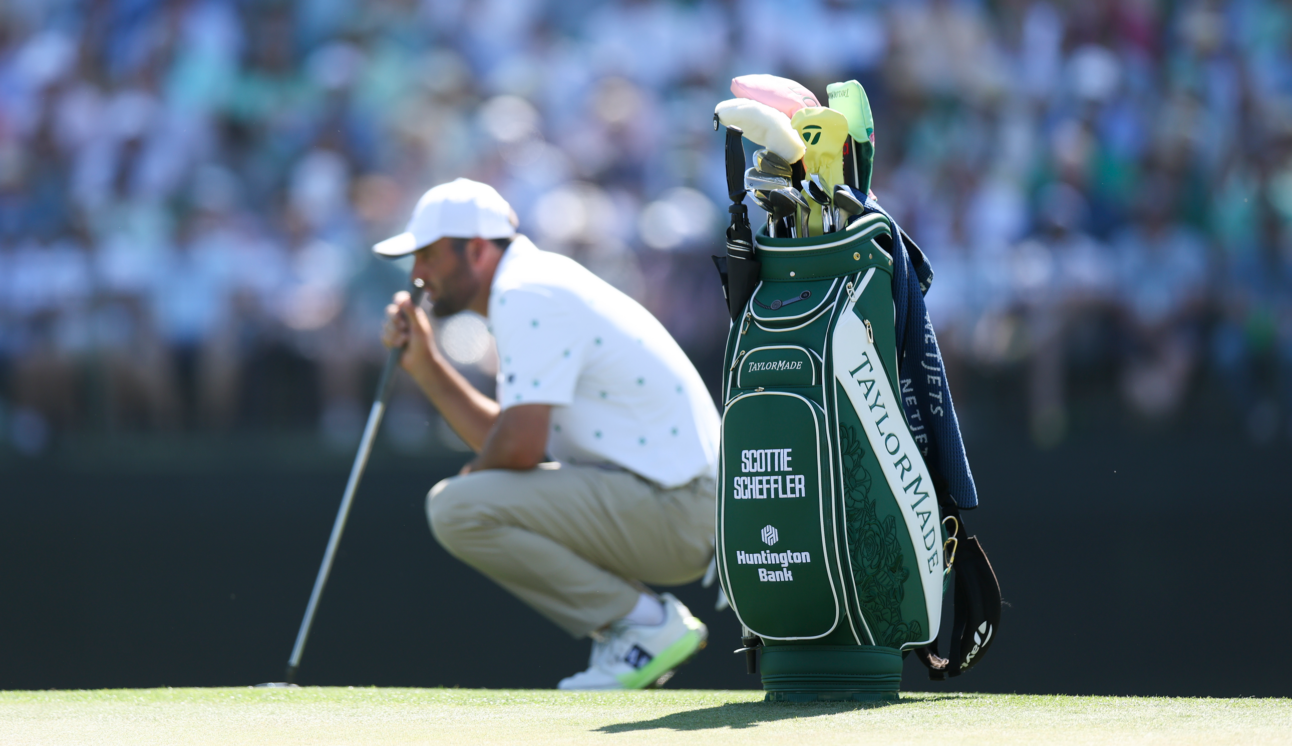 Scottie Scheffler lines up a putt, with his bag standing behind him