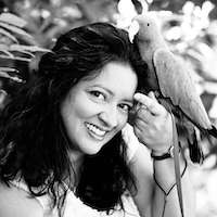 a black and white photo of bird expert, Monika Sangar sat holding a parrot outside