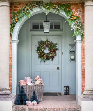 home exterior with front door painted light blue, arched entrance with foliage garland, front door festive wreath and lantern hanging from the porch roof