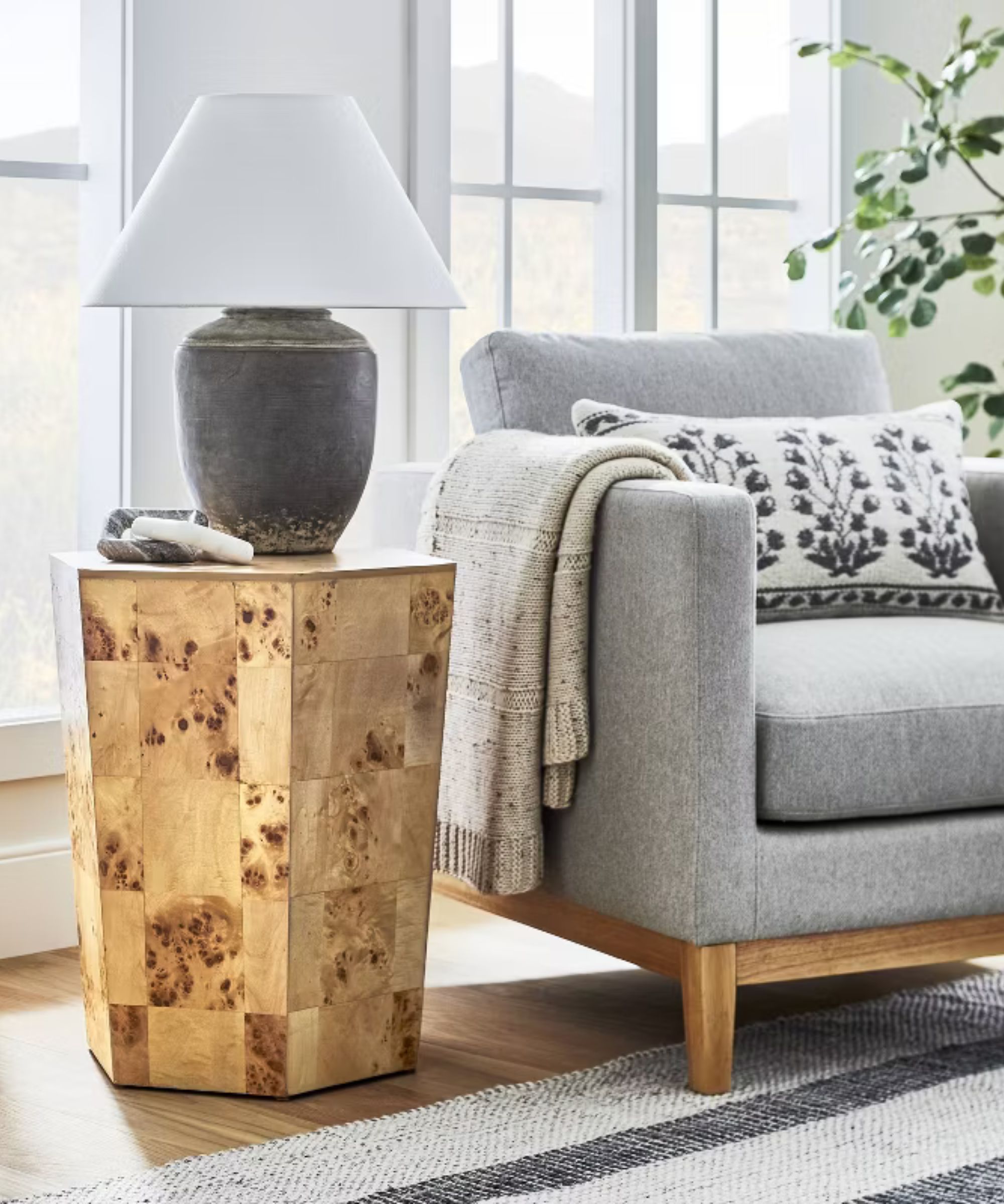 Burl wood side table next to a grey armchair with a gray stone lamp on top