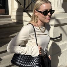 Woman wears white top, black trousers and carries black woven leather bag