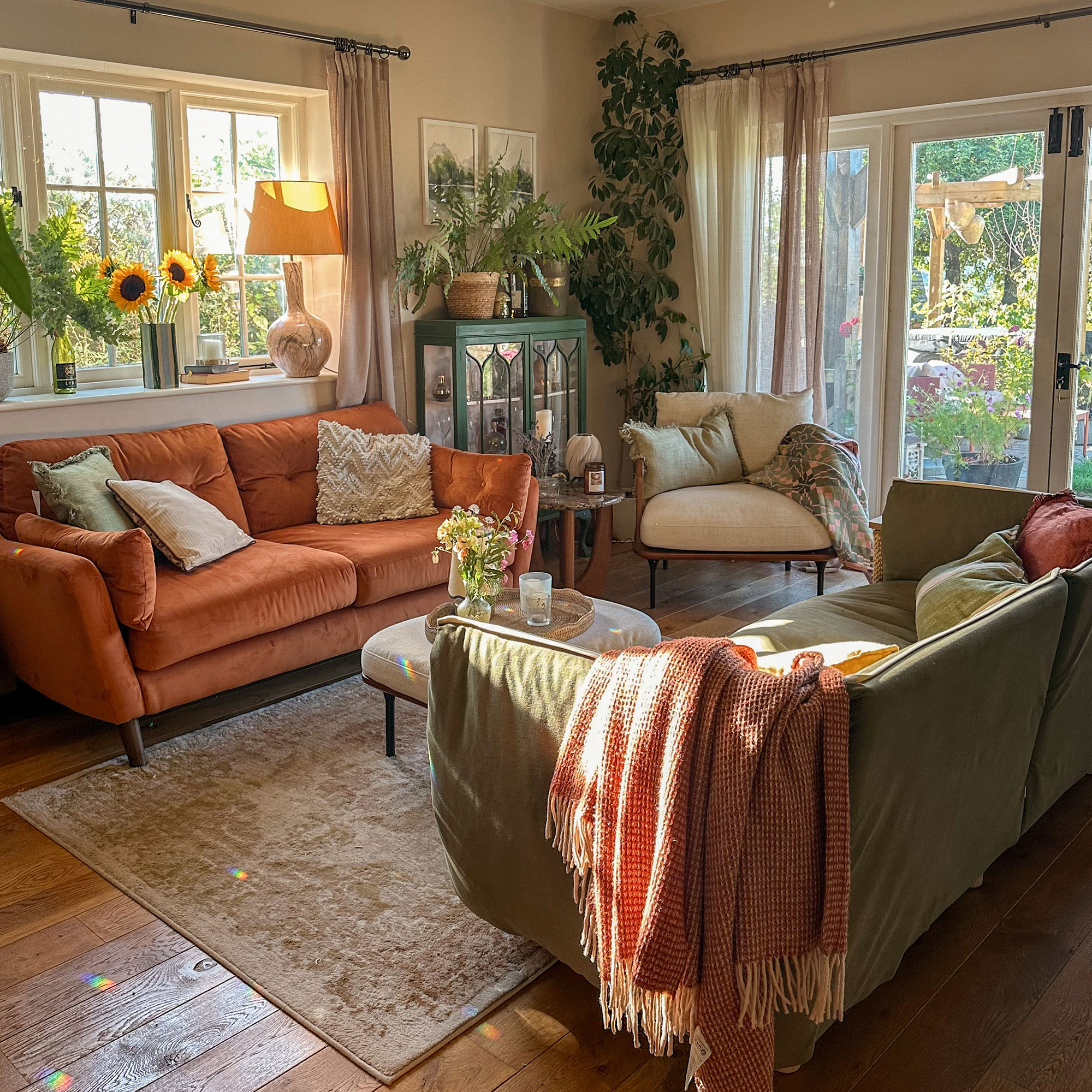 Living room with neutral walls, wooden floors, patterned rug and orange sofa facing sage green sofa