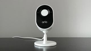 En Arlo Essential Indoor Camera står på en svart yta med kameralinsen vänd mot kameran.