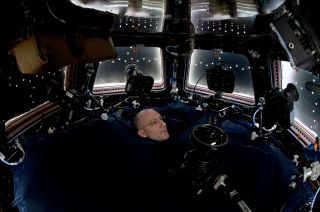 Astronaut Don Pettit's head pops through a cloth barrier blocking stray light from entering the International Space Station's Cupola module as he photographs Earth from orbit.