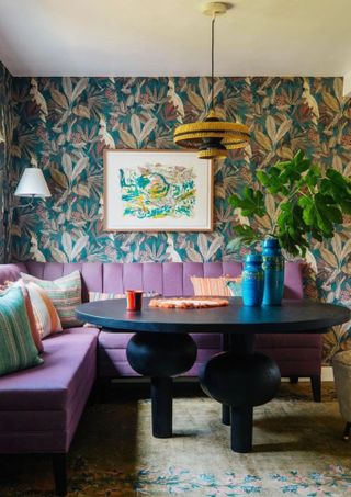colorful dining room with purple sofa, black table and botanical wallpaper