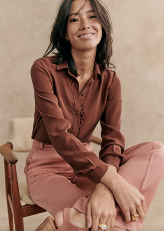 a model wears a sezane shirt sitting in front of a plain backdrop