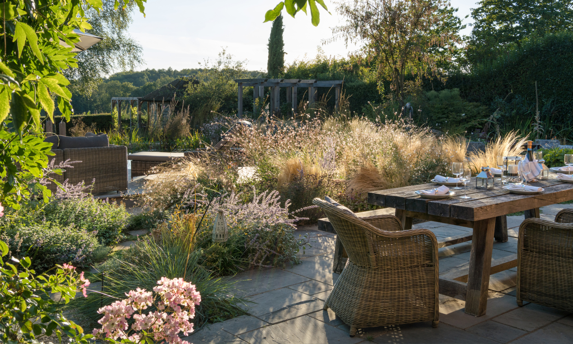 Autumnal garden landscape with ornamental grasses, gaura, and a patio table with large wicker chairs