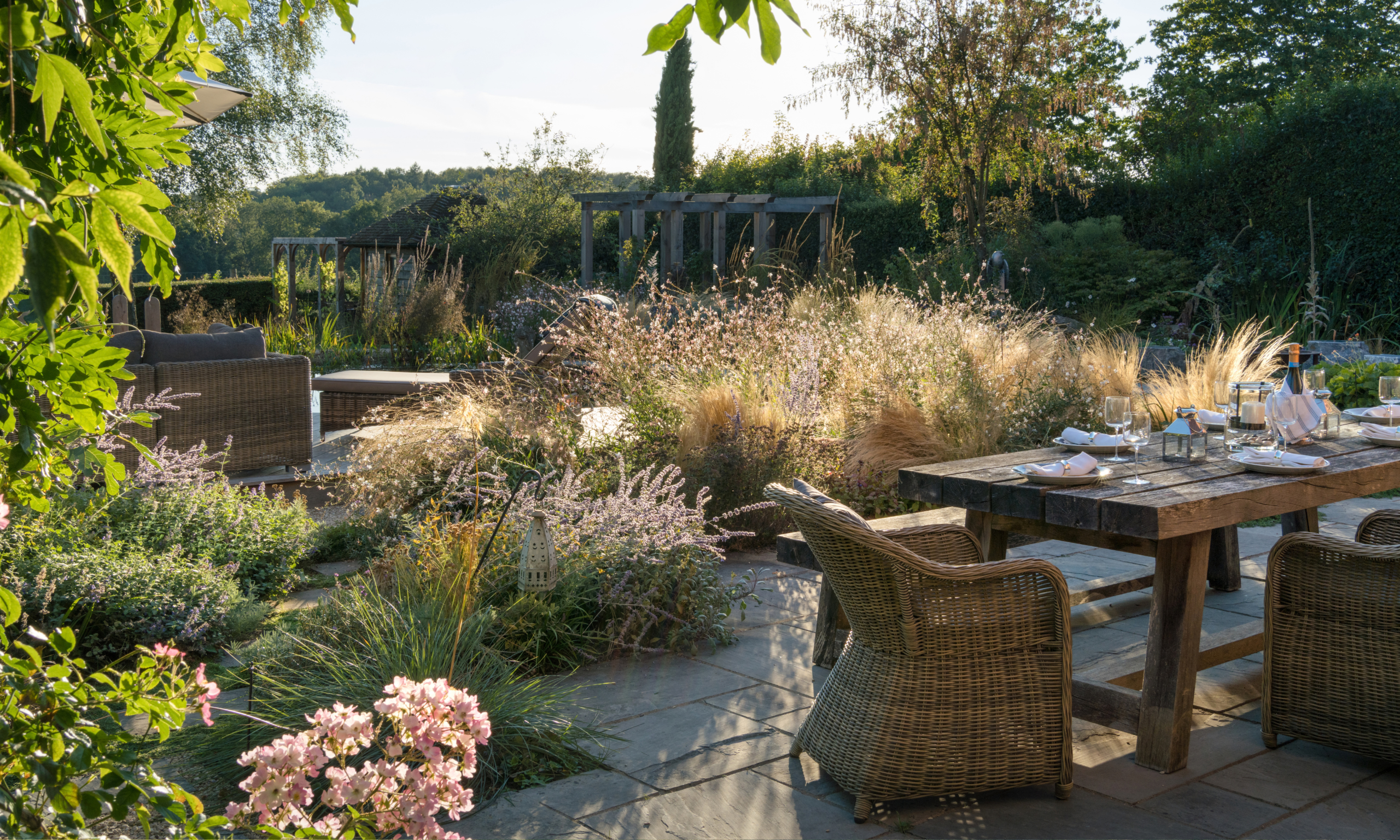 Autumnal garden landscape with ornamental grasses, gaura, and a patio table with large wicker chairs