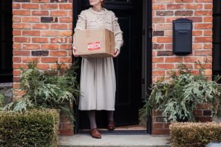 Kvinde med pakke i hænderne ude foran sit hjem