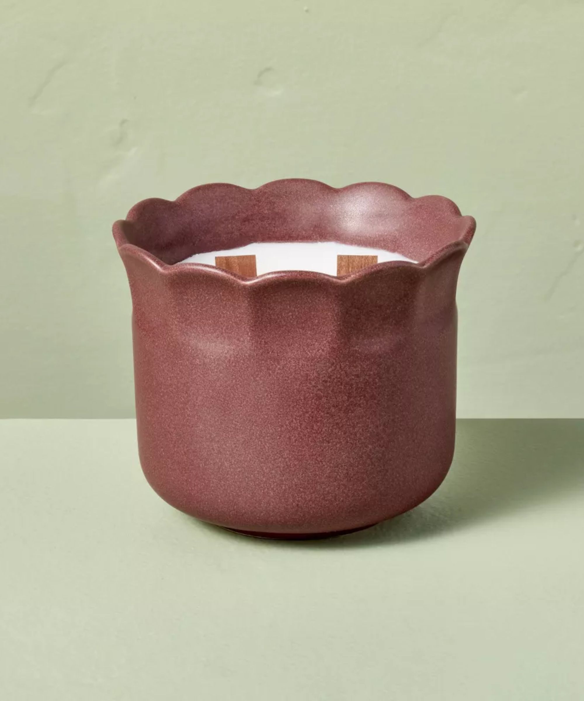 White candle with 2 wooden wicks, in a scalloped burgundy jar, against a mint green background.