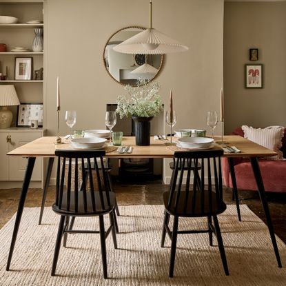 A neutral shade-painted dining room with a set dining table with Scandi-style black chairs and a small flower arrangement as a centrepiece