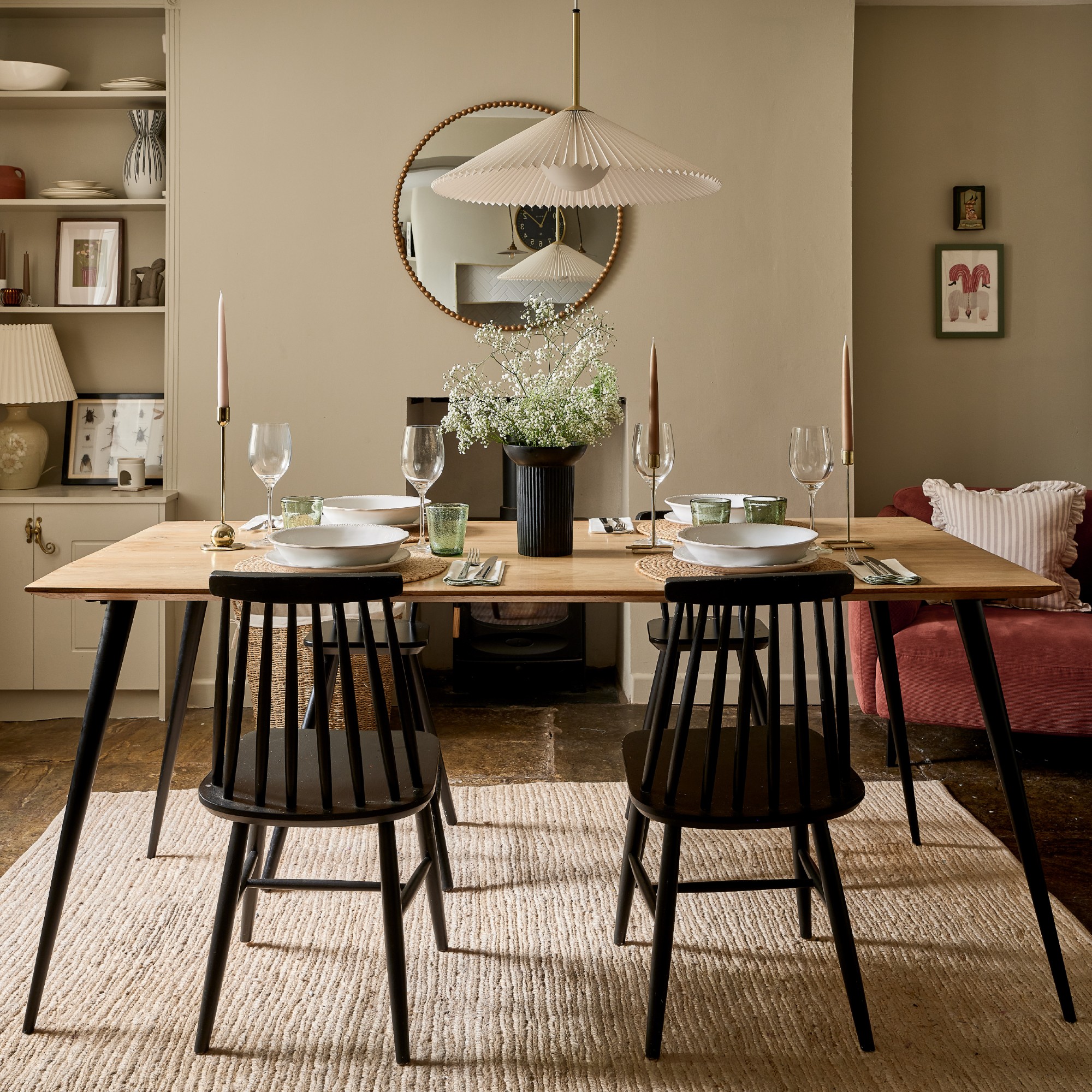 A neutral shade-painted dining room with a set dining table with Scandi-style black chairs and a small flower arrangement as a centrepiece