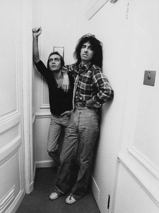 Alice Cooper and Bernie Taupin lean on each other in a corridor