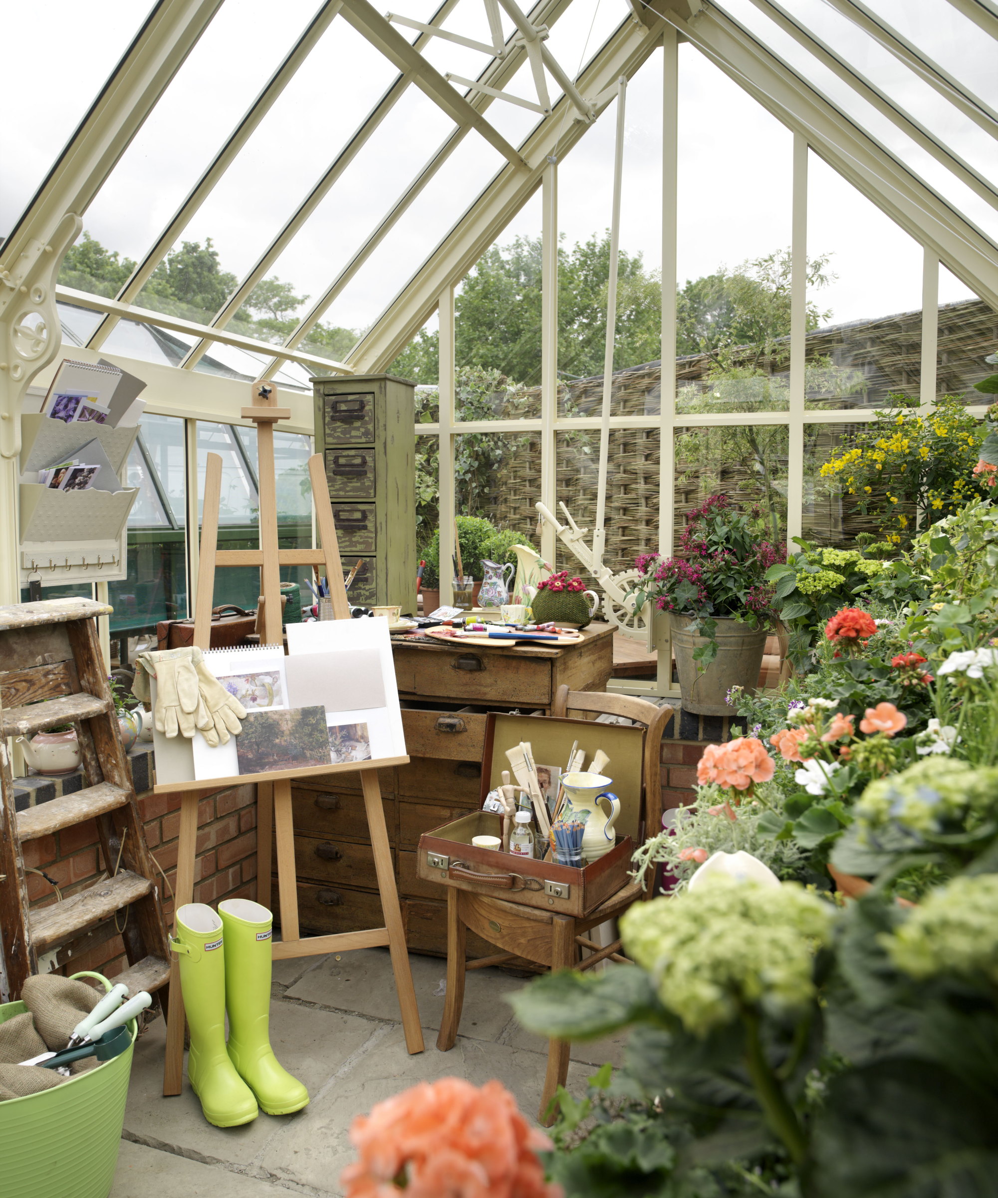 A greenhouse potting shed is filled with plants and a desk, set up as an artist's studio