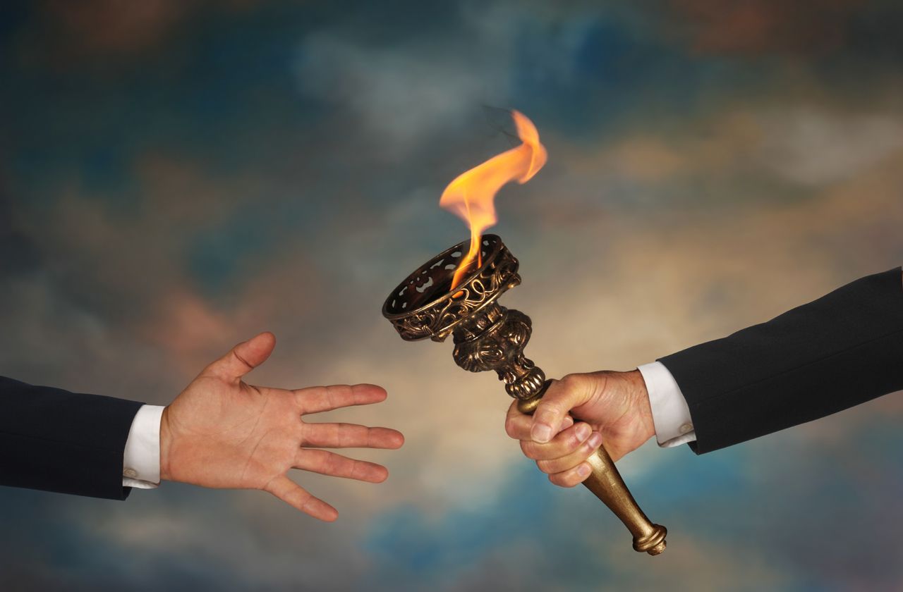 Businessman&amp;#039;s outstretched arm passing a flaming torch to another businessman&amp;#039;s open hand