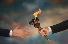 Businessman's outstretched arm passing a flaming torch to another businessman's open hand