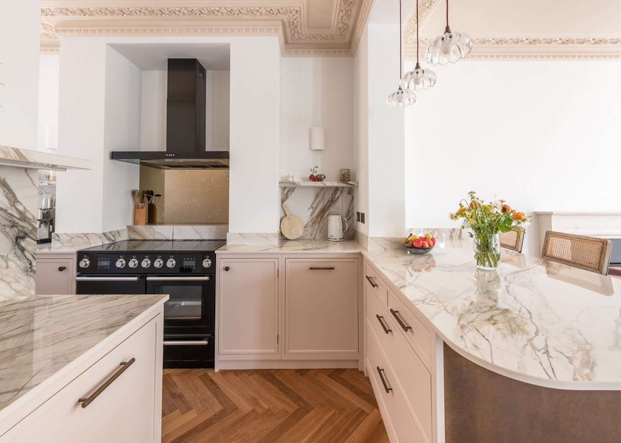 A curved peninsula unit with a marble countertop. There are flowers on the island with a vase. There is also a view of the rest of the kitchen