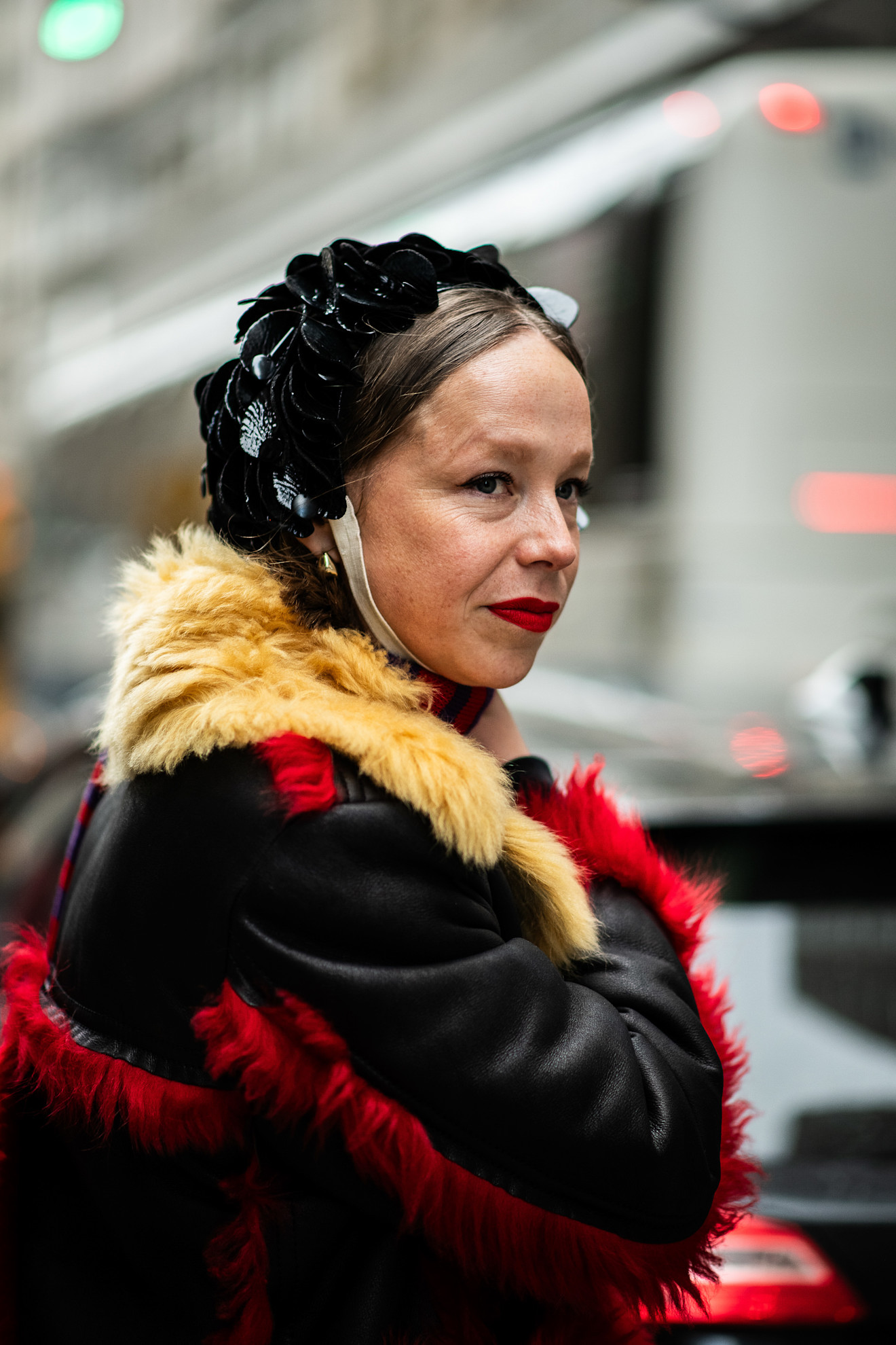 a woman in a black, tan, and red jacket with a black hat and red lipstick
