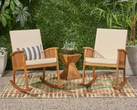 A pair of wooden outdoor rocking chairs with cream upholstered cushions in a leafy backyard